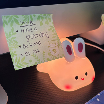 A sticky note pad with a leafy border and a to-do list sits next to a bunny lamp.