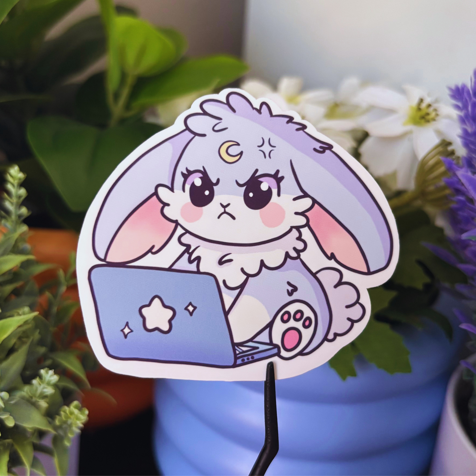 A grumpy purple bunny sticker with a crescent moon on its forehead types on a laptop.