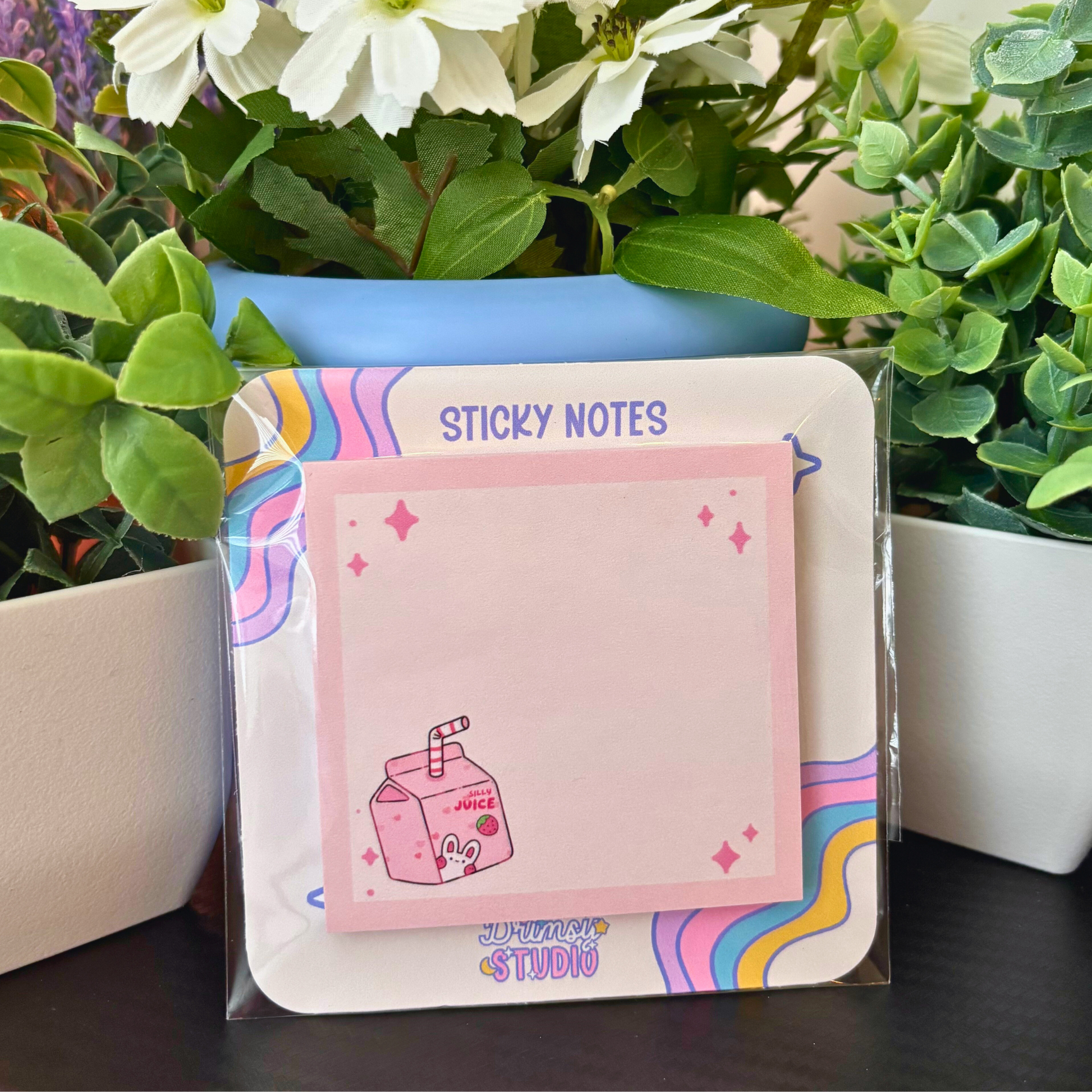 Pink sticky notes with a juice box design are displayed among green plants.