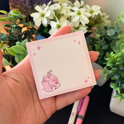 Pink sticky note pad with a cartoon juice box and stars, held in a hand.