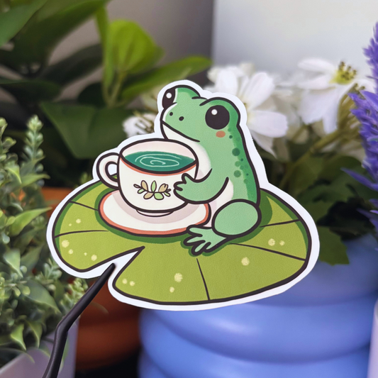 Frog Tea Time Sticker featuring a frog holding a teacup on a lily pad.